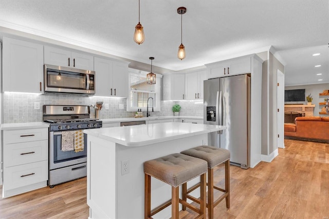 kitchen with a kitchen island, light countertops, light wood-style flooring, stainless steel appliances, and a sink