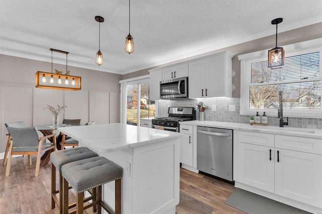 kitchen with light wood finished floors, backsplash, a kitchen island, stainless steel appliances, and a sink