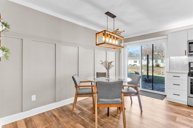 dining space featuring light wood-style flooring, ornamental molding, a textured ceiling, wainscoting, and a decorative wall