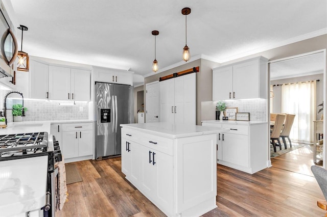 kitchen featuring a sink, wood finished floors, a barn door, appliances with stainless steel finishes, and crown molding