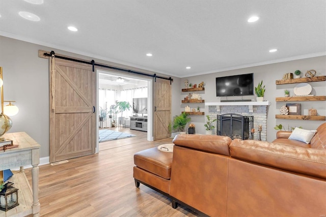 living room with light wood-type flooring, recessed lighting, a barn door, crown molding, and a brick fireplace