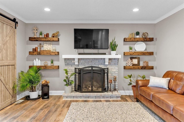 living room featuring ornamental molding, a fireplace, a barn door, and wood finished floors