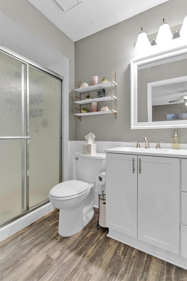 full bath with toilet, a stall shower, a textured ceiling, and wood finished floors