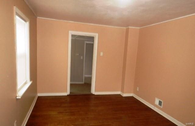 spare room with ornamental molding, wood finished floors, visible vents, and baseboards