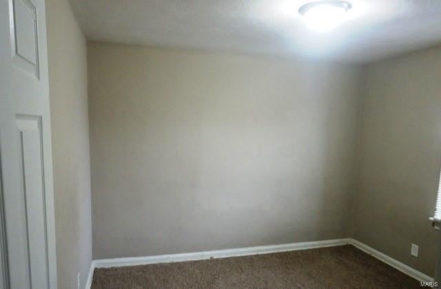 unfurnished room featuring baseboards and dark colored carpet