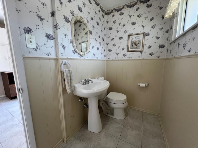 half bathroom featuring wainscoting, toilet, tile patterned floors, and a sink
