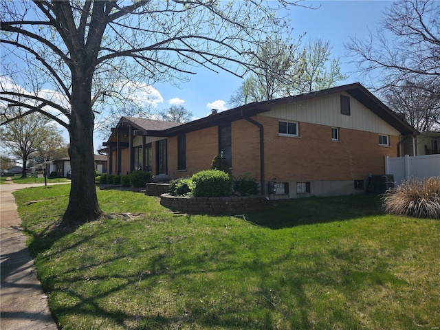view of property exterior with fence, a lawn, and brick siding