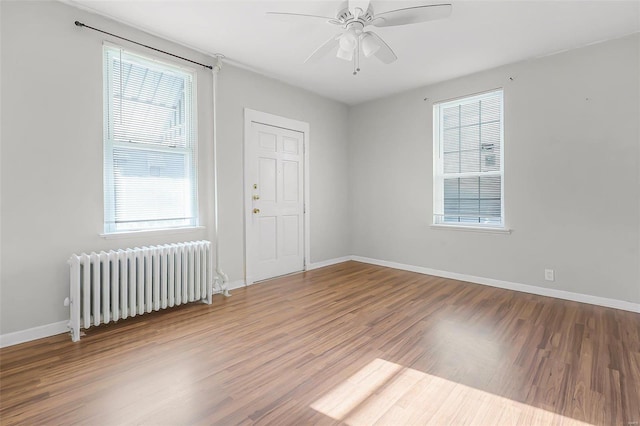 empty room featuring ceiling fan, radiator, baseboards, and wood finished floors