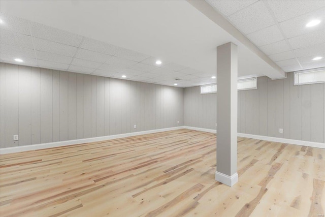 below grade area with recessed lighting, a paneled ceiling, baseboards, and wood finished floors