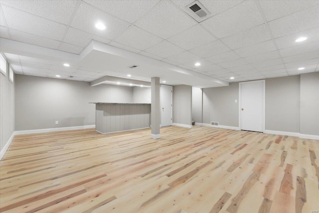 finished basement featuring a paneled ceiling, wood finished floors, visible vents, and baseboards