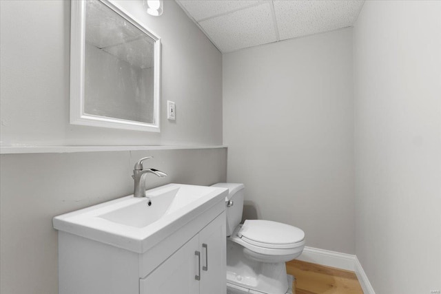 bathroom featuring baseboards, a drop ceiling, toilet, wood finished floors, and vanity