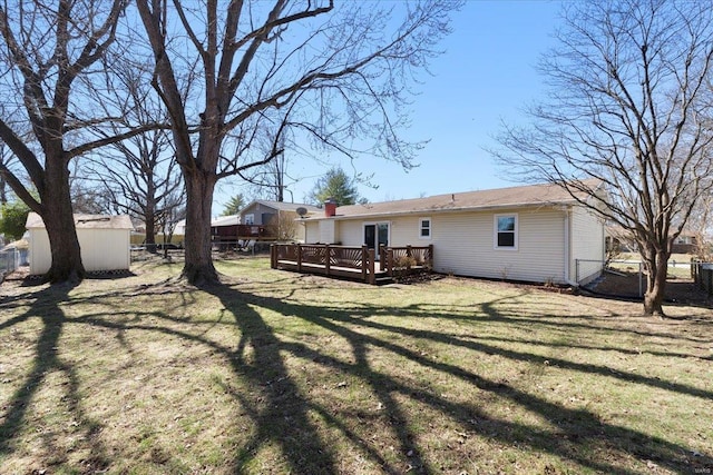 rear view of property with an outbuilding, fence, a storage unit, a deck, and a lawn