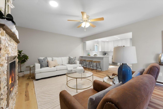 living room featuring baseboards, ceiling fan, recessed lighting, light wood-style flooring, and a fireplace