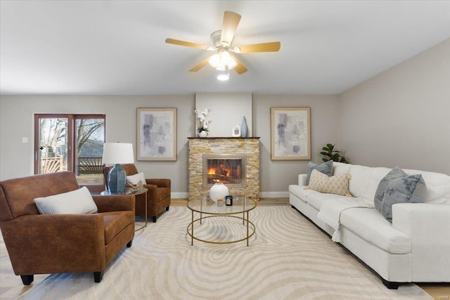 living room featuring a stone fireplace, baseboards, a ceiling fan, and wood finished floors