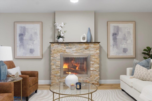 living area featuring a stone fireplace, baseboards, and wood finished floors