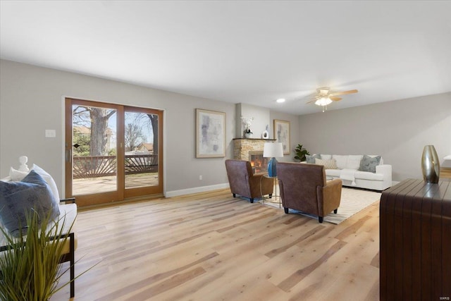 living room with a stone fireplace, light wood-style floors, baseboards, and a ceiling fan