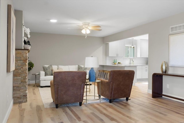 living room with light wood finished floors, visible vents, baseboards, and a ceiling fan