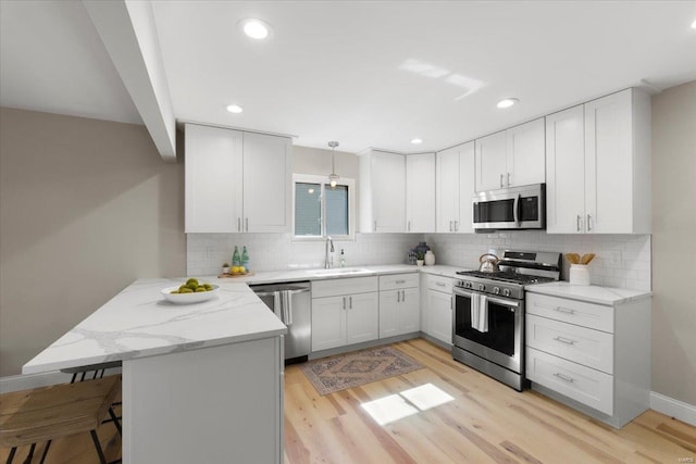 kitchen featuring light stone countertops, appliances with stainless steel finishes, a peninsula, light wood-style floors, and a sink