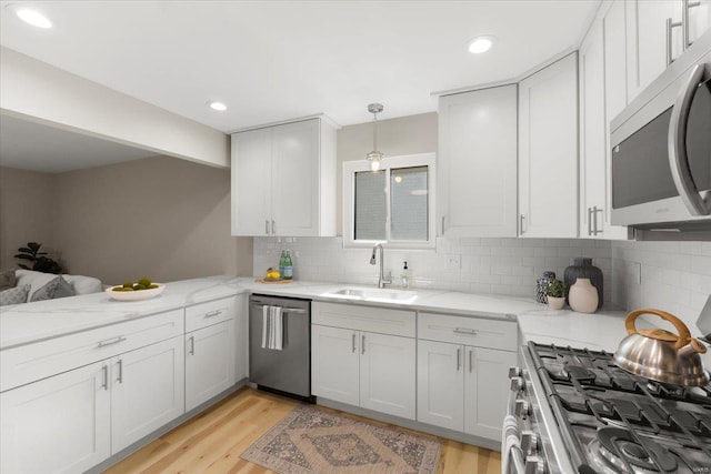 kitchen with light wood finished floors, light stone countertops, decorative backsplash, appliances with stainless steel finishes, and a sink