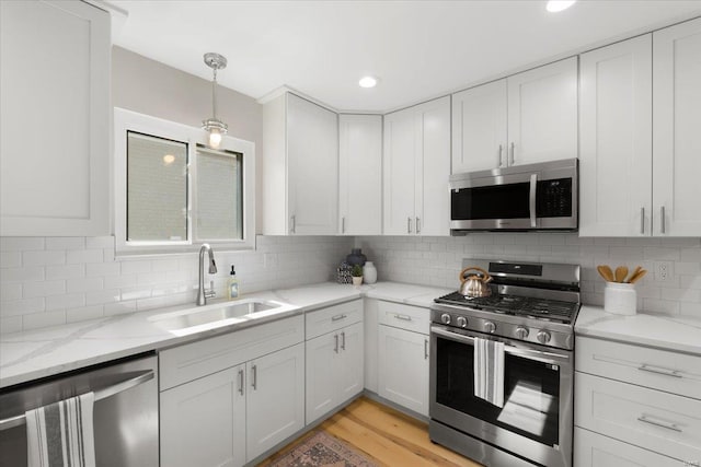 kitchen featuring light wood finished floors, backsplash, appliances with stainless steel finishes, white cabinets, and a sink