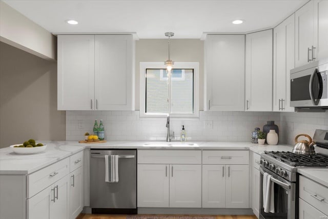 kitchen featuring a sink, white cabinetry, stainless steel appliances, a peninsula, and decorative backsplash