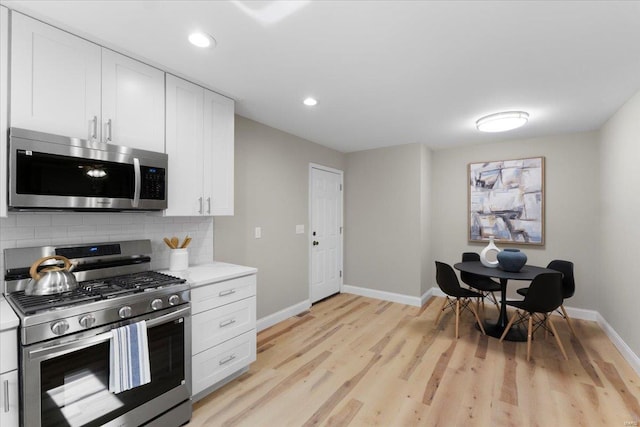 kitchen featuring baseboards, light wood-style flooring, decorative backsplash, white cabinets, and appliances with stainless steel finishes