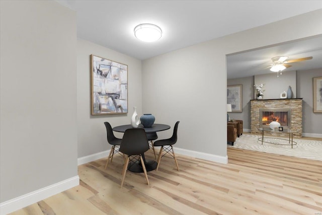 dining room featuring a fireplace, a ceiling fan, light wood-type flooring, and baseboards