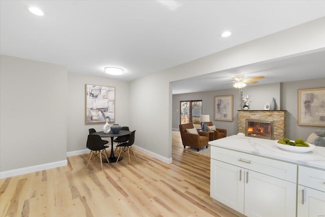 kitchen with white cabinetry, a stone fireplace, light wood finished floors, baseboards, and light stone countertops