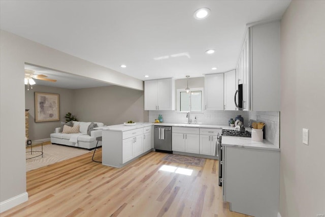 kitchen with a peninsula, stainless steel appliances, open floor plan, light wood-type flooring, and backsplash