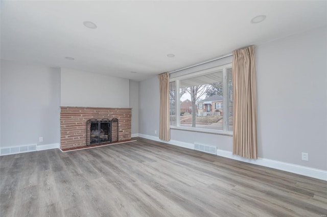 unfurnished living room featuring a brick fireplace, visible vents, baseboards, and wood finished floors