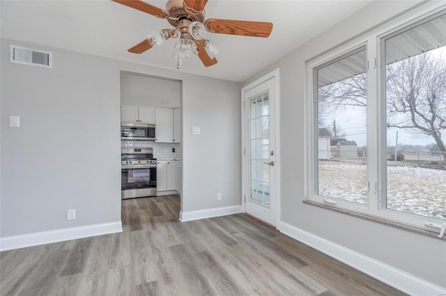 unfurnished dining area with ceiling fan, light wood-type flooring, visible vents, and baseboards