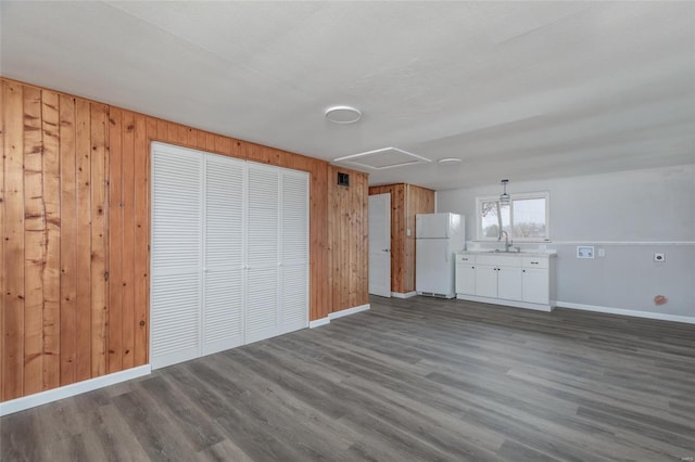 unfurnished living room featuring a sink, wood walls, baseboards, and dark wood-type flooring