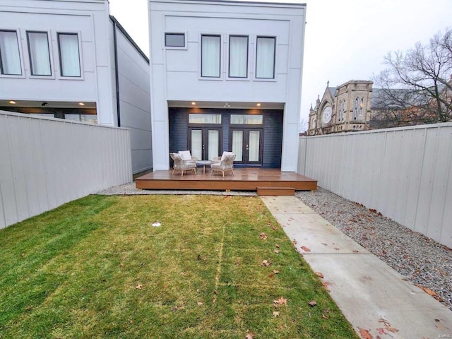 rear view of house with stucco siding, a lawn, a fenced backyard, french doors, and a wooden deck