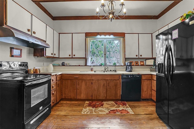 kitchen featuring hardwood / wood-style flooring, under cabinet range hood, light countertops, black appliances, and a notable chandelier