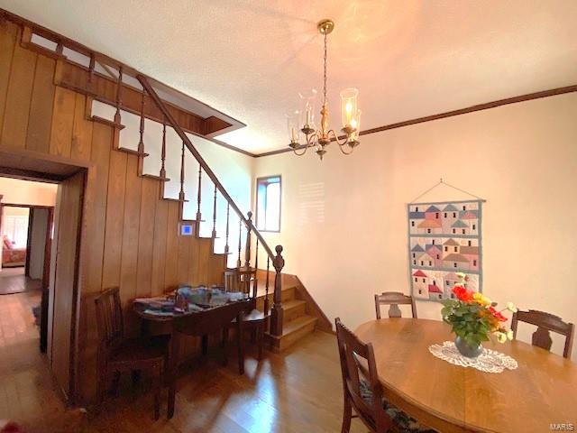 dining room featuring wooden walls, stairs, wood finished floors, and an inviting chandelier