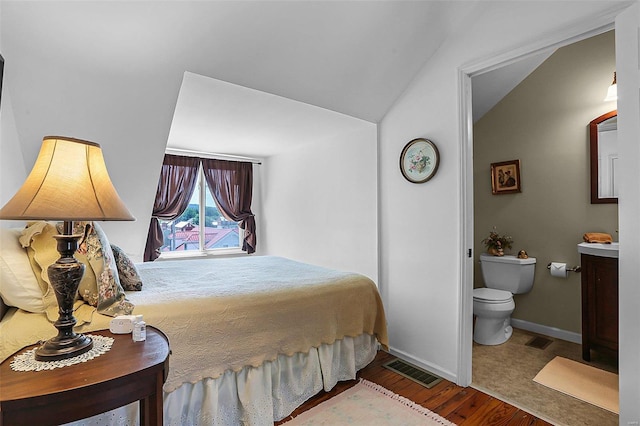 bedroom with lofted ceiling, connected bathroom, wood finished floors, visible vents, and baseboards