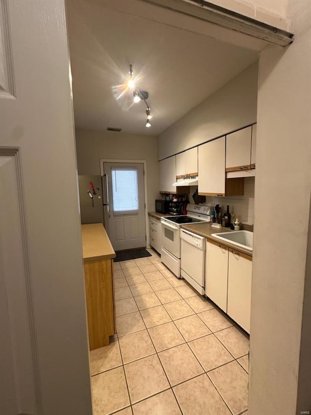 kitchen with light tile patterned floors, under cabinet range hood, white appliances, a sink, and white cabinets