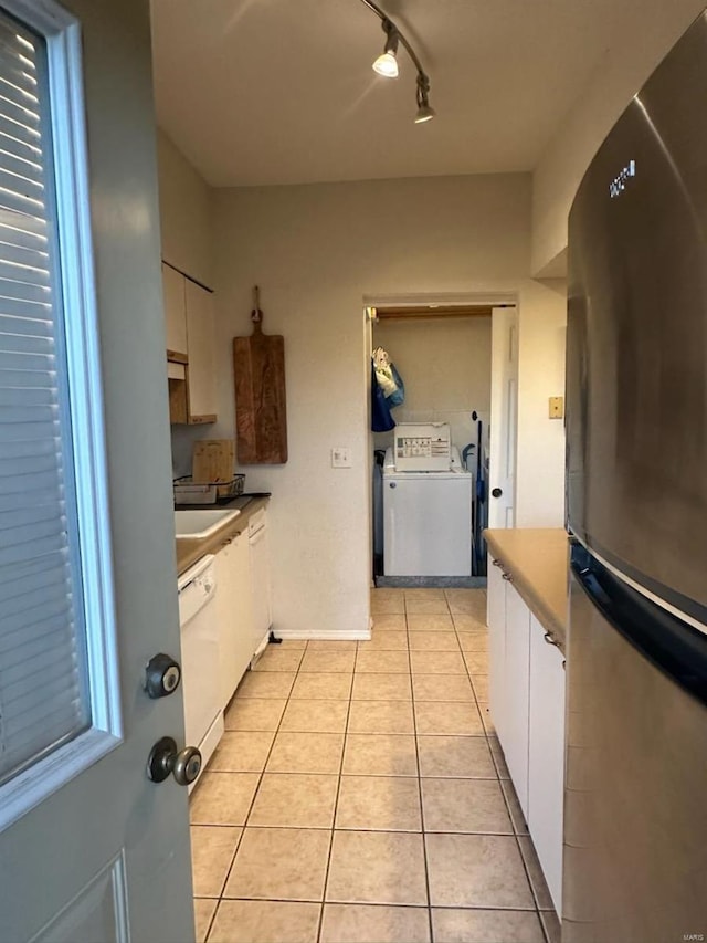 kitchen featuring light tile patterned floors, white dishwasher, white cabinets, freestanding refrigerator, and washer / dryer