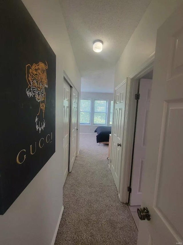 corridor featuring a textured ceiling, baseboards, and light colored carpet