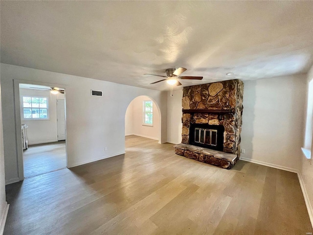 unfurnished living room featuring arched walkways, a fireplace, wood finished floors, and a wealth of natural light