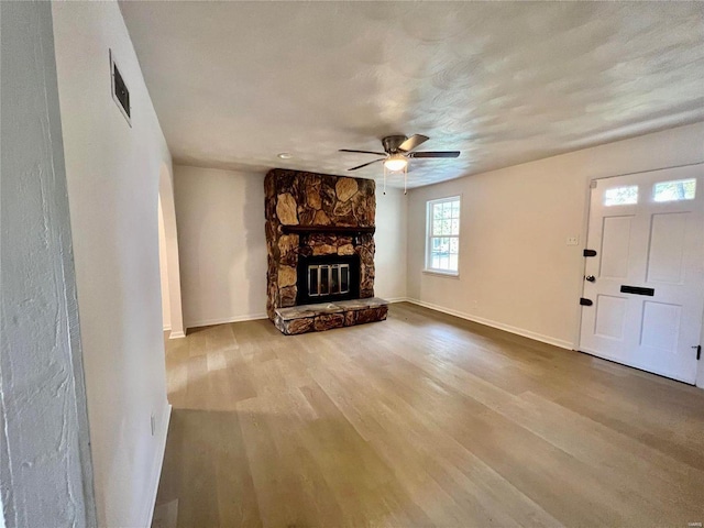 unfurnished living room featuring visible vents, a ceiling fan, a stone fireplace, wood finished floors, and baseboards