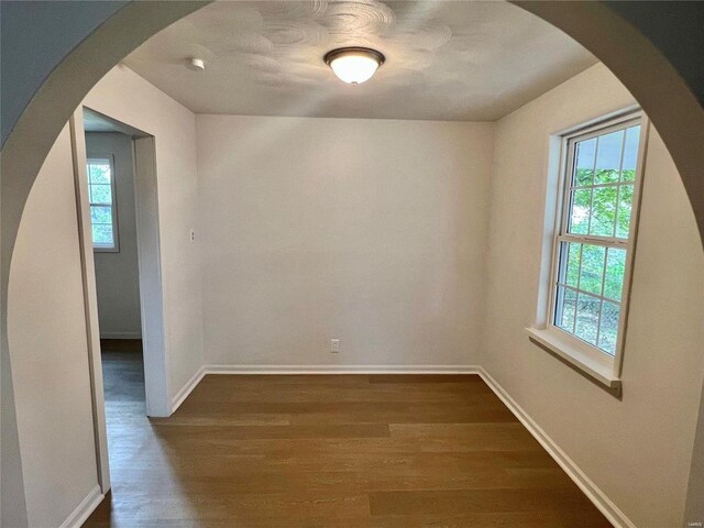 empty room featuring dark wood-style floors, plenty of natural light, arched walkways, and baseboards