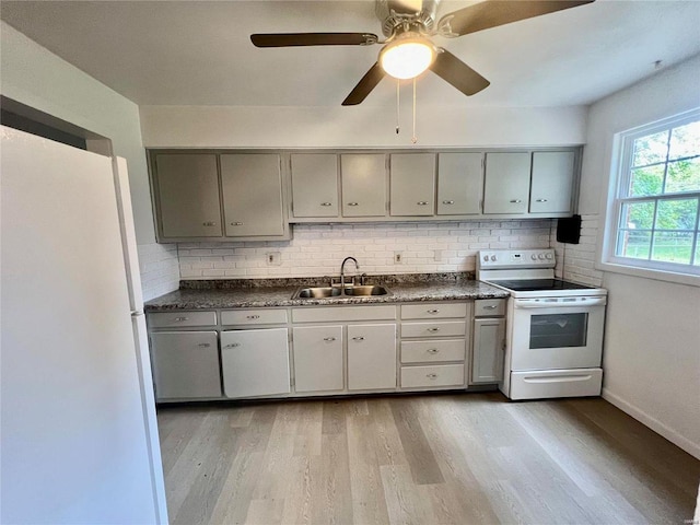 kitchen featuring light wood-style flooring, gray cabinetry, white appliances, a sink, and dark countertops