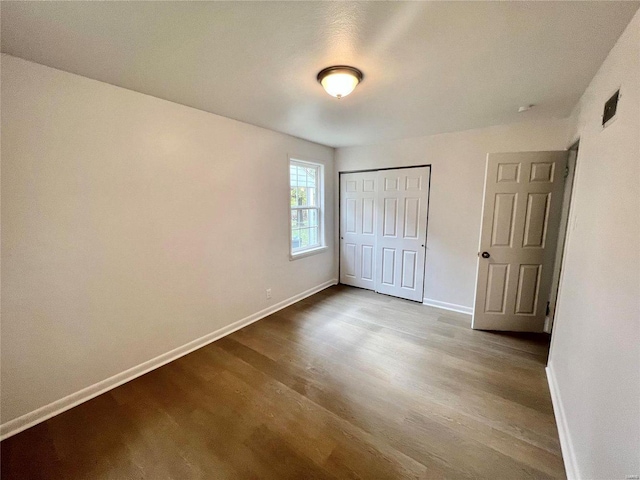 unfurnished bedroom with baseboards, dark wood finished floors, and a closet