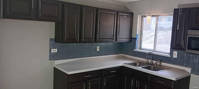 kitchen with hanging light fixtures, light countertops, a sink, and backsplash