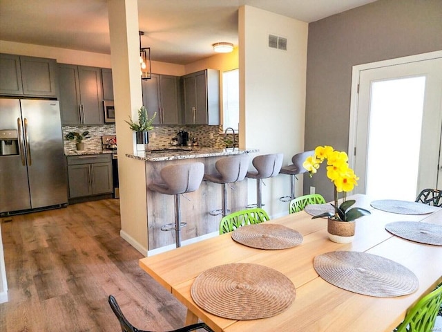 kitchen with visible vents, backsplash, appliances with stainless steel finishes, wood finished floors, and a kitchen bar