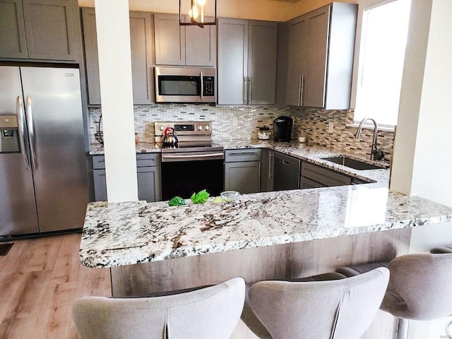 kitchen featuring light stone counters, stainless steel appliances, backsplash, a sink, and light wood-type flooring