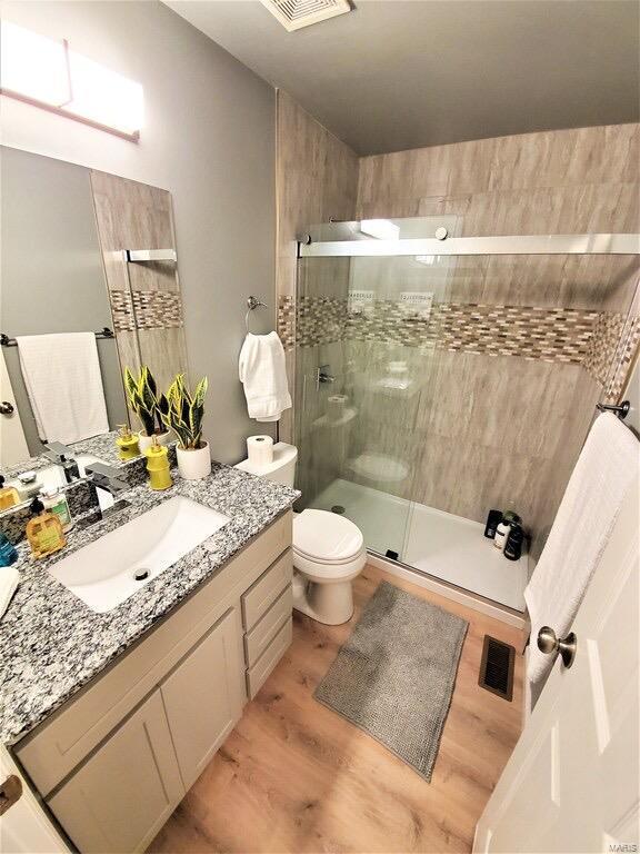 full bathroom with toilet, wood finished floors, vanity, visible vents, and a shower stall