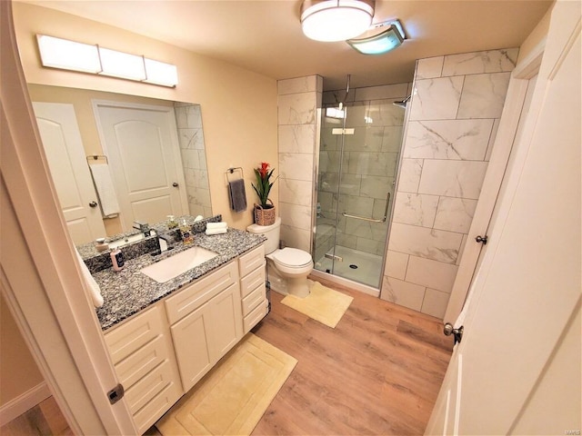 bathroom with toilet, a shower stall, wood finished floors, and vanity