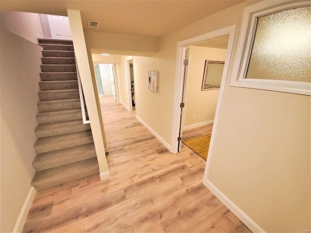 corridor featuring baseboards, stairway, visible vents, and light wood-style floors